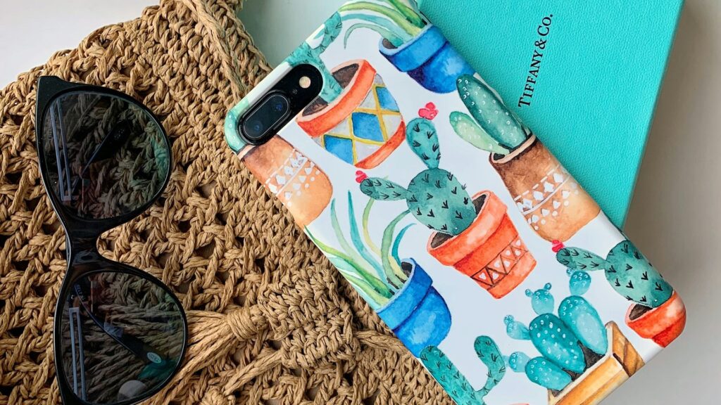 Telefoonhoesje met handgetekende cactusprint ligt op gevlochten tas naast zonnebril